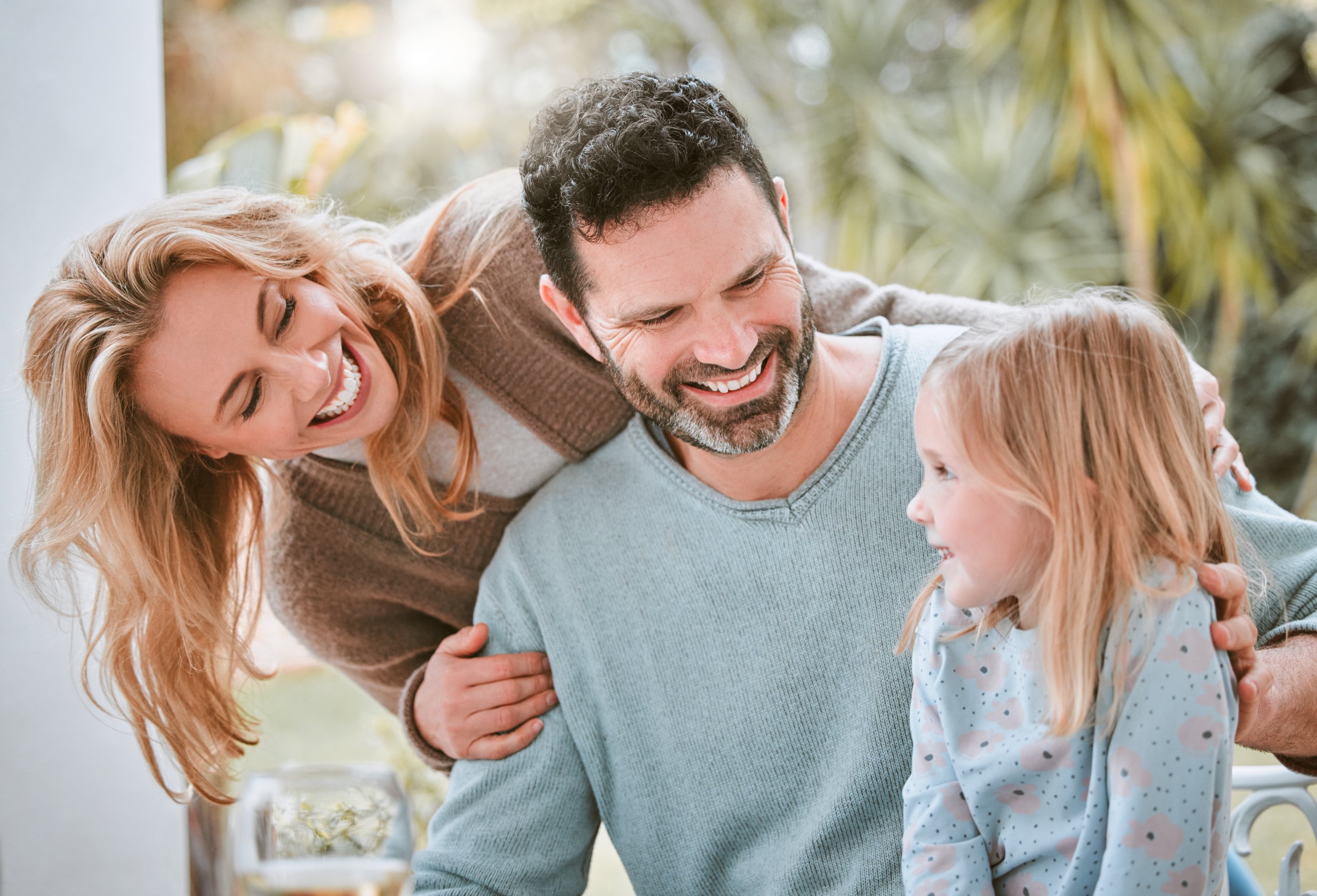 A smiling mother, father and young daughter sharing a laugh outdoors