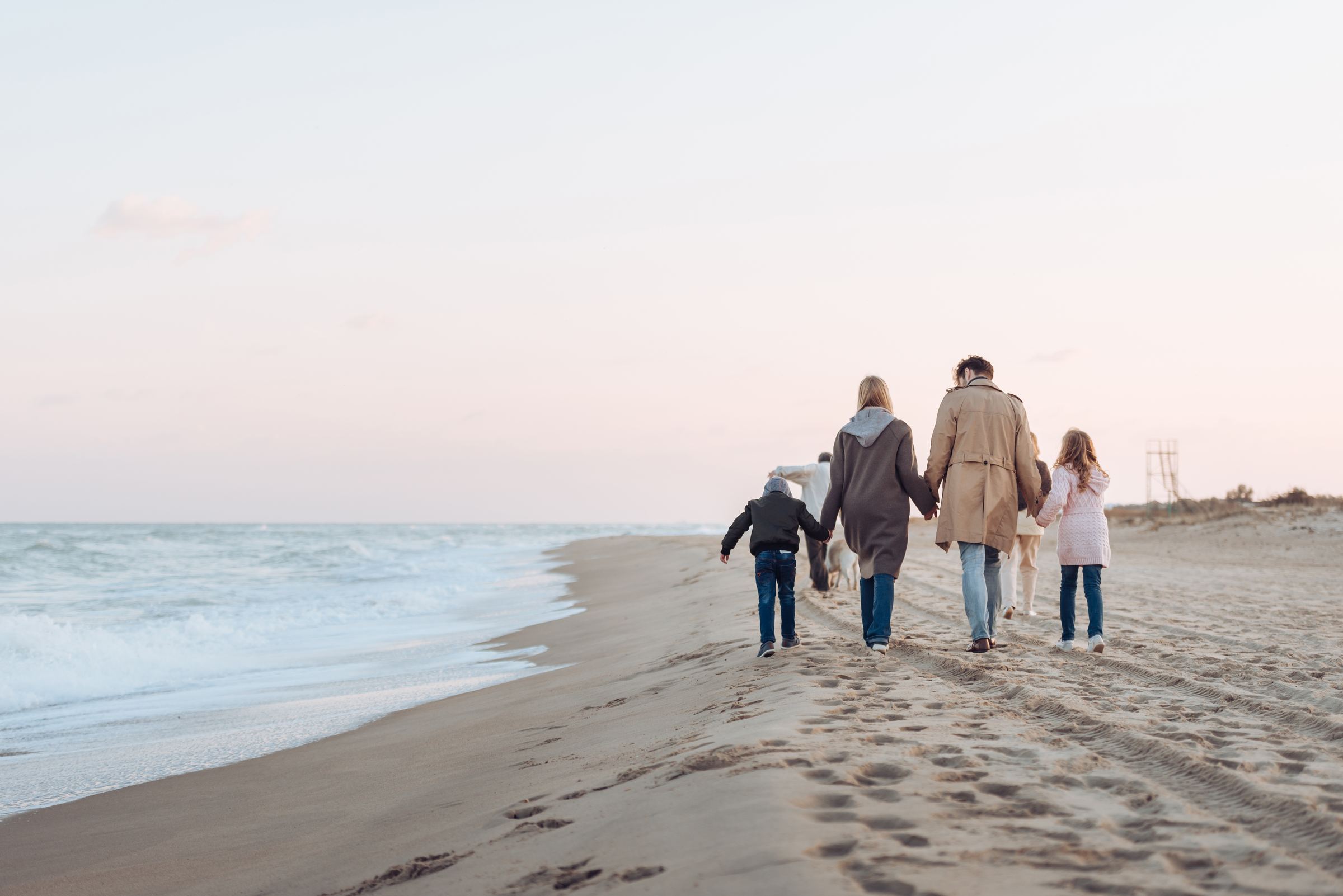 A family walking hand in hand along the beach at sunset